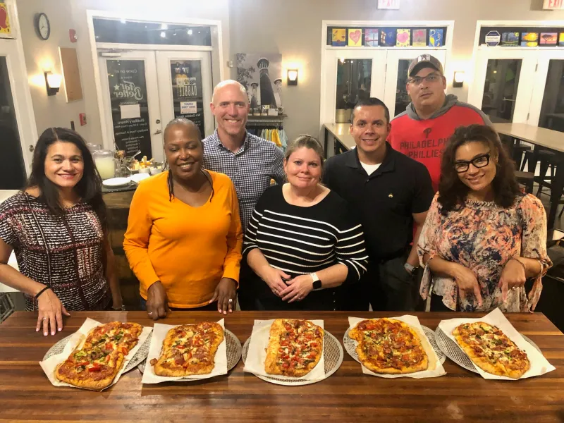 a group of people sitting at a table eating pizza posing for the camera